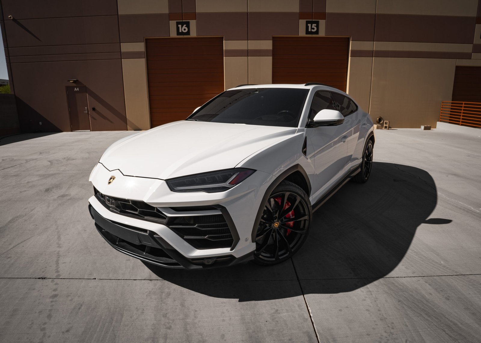 Lamborghini Urus luxury SUV in white, showcasing sleek design and bold features, parked in front of industrial garage doors in Scottsdale, Arizona, highlighting exotic car rental options.
