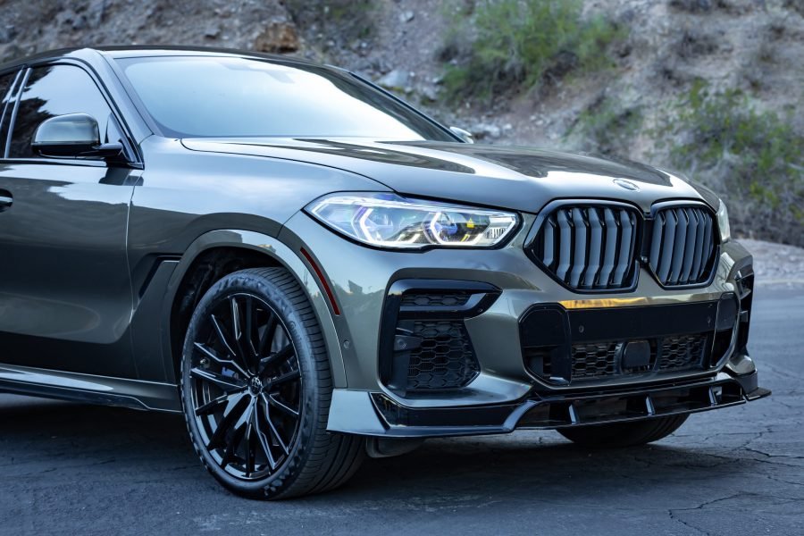 BMW X6 M50i in sleek gray exterior, showcasing aggressive front grille, sporty design, and black alloy wheels, set against a natural backdrop, emphasizing luxury and performance features for rental.