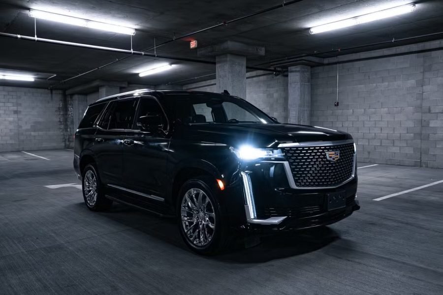 Cadillac Escalade SUV parked in a dimly lit garage, showcasing luxury design, chrome wheels, and distinctive front grille.